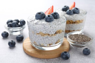 Chia tohumlu lezzetli puding, yoğurt, yaban mersini, granola ve çilek açık gri masada, yakın plan. Süper yemek.