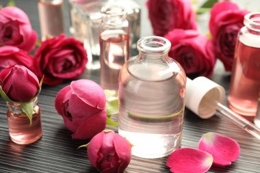 Aromatik esanslı parfüm şişelerini aç ve gri ahşap masada güller, yakın plan.