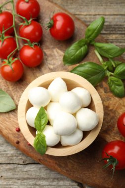 Lezzetli mozzarella peynir topları kasede, fesleğende, biberlikte ve domateslerde ahşap masada, üst tarafta.