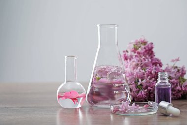 Lüks parfüm yapıyorum. Temel yağlar cam süslemede ve çiçekler açık ahşap masada, yakın plan. Metin için boşluk