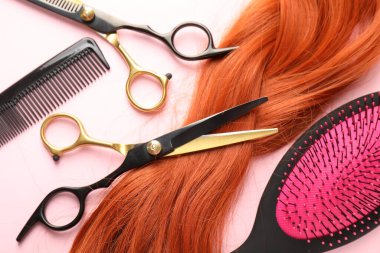 Açık pembe zemin üzerinde saç teli ve kuaför aletleri, düz uzanma