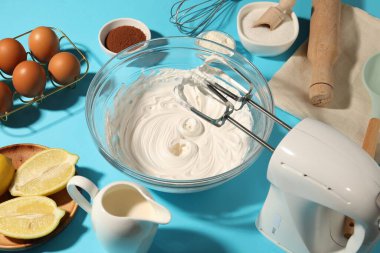 Açık mavi masada çırpılmış krema, yumurta ve diğer ürünlerle karıştırıcı, yakın plan.