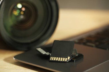 SD hafıza kartları, dizüstü bilgisayar ve fotoğraf makinesi ahşap masada, yakın plan.