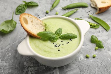 Lezzetli bezelye kremalı çorba fesleğen ve kızarmış ekmek, yakın plan, gri masada servis edilir.