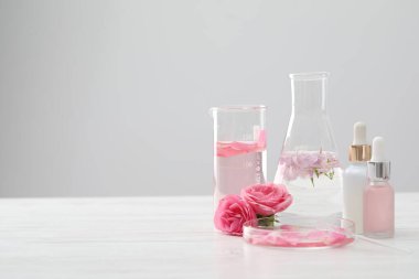 Lüks parfüm yapıyorum. Temel yağlar cam süslemede ve çiçekler beyaz ahşap masada, yakın plan. Metin için boşluk