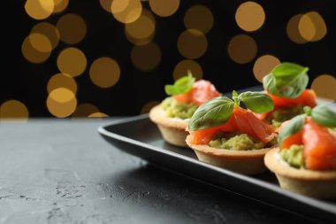 Siyah masadaki lezzetli kanepeler karanlık arka planda bulanık ışıklarla, yazı için yer açıyorlar. Bokeh etkisi