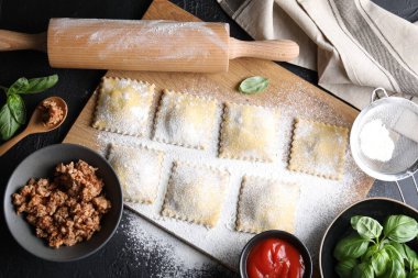 Pişmemiş ravioli, merdane, bolonez, sos ve fesleğen siyah masada, düz yatıyordu.
