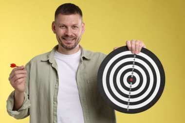 Hedef alınıyor. Sarı arka planda ok ve dart tahtası olan adam.