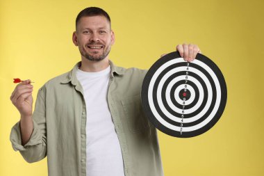 Hedef alınıyor. Sarı arka planda ok ve dart tahtası olan adam.