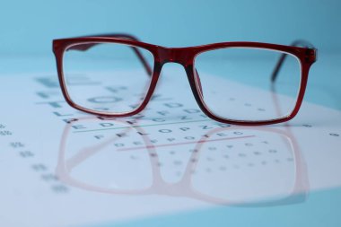 Açık mavi arkaplanda gözlük ve görüş testi grafiği, yakın plan