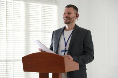 İçerideki kürsüde mikrofonla halka açık konuşma yapan adam.