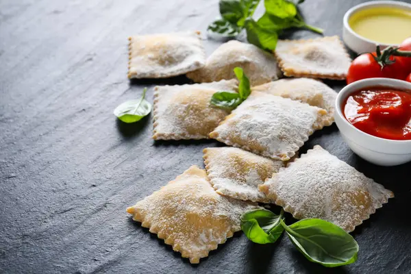 Pişmemiş ravioli, sos, domates ve fesleğen siyah masada, yakın plan.