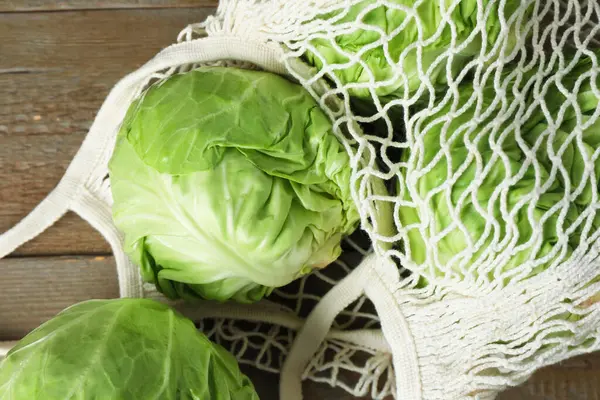 Taze lahanalar ve ahşap masada ağ torba, yakın plan.