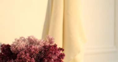 Tuvaletteki şifoniyerde temiz waffle havluları ve vazo dolusu leylak çiçekleri, mesaj için yer. Kamera aşağı iniyor