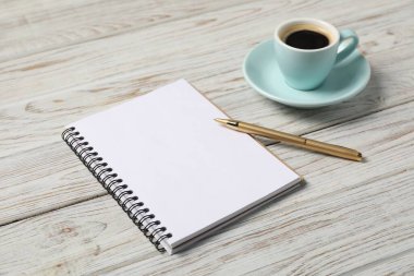 Beyaz ahşap masanın üzerinde kalem ve kahve olan defter, yakın plan.