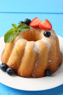 Açık mavi ahşap masada pudra şekerli ve dutlu Lezzetli kek, yakın plan.