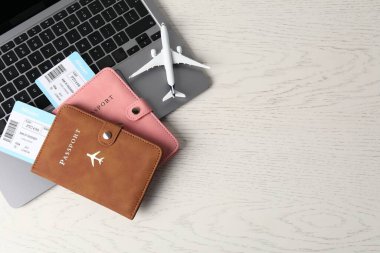 Pasaportlar, uçuş biletleri, uçak modeli ve laptop beyaz ahşap masa, üst manzara. Metin için boşluk
