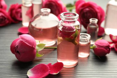 Aromatik esanslı parfüm şişelerini aç ve gri ahşap masada güller, yakın plan.