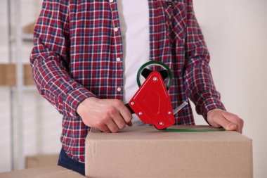 Karton kutuyu kapalı bir yere kapatmak için yapıştırıcılı bant kullanan bir adam.