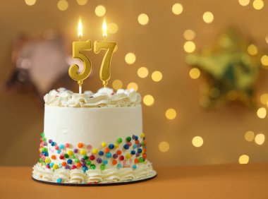 Bulanık ışıklara karşı yanan mumları olan nefis bir pasta, yazı için yer. 57. yaş günü veya diğer özel günler