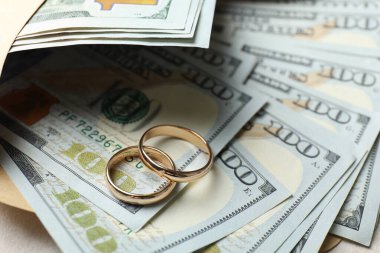 İki altın alyans, bir dolarlık banknotlar ve beyaz masanın üzerindeki zarf, yakın plan.