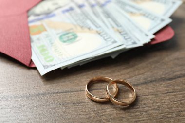 Altın alyanslar, zarf ve dolar banknotları ahşap masada, yakın plan.