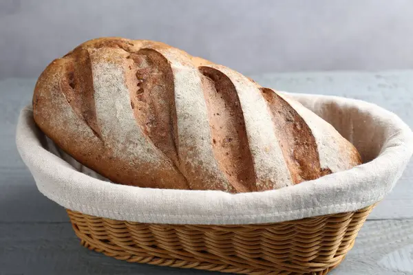 Gri ahşap masadaki sepetin içinde bir somun ekmek, yakın plan.