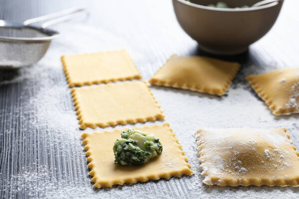 Making ravioli with cottage cheese and spinach at wooden table, closeup