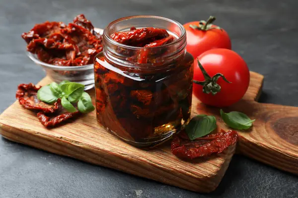 Lezzetli güneşte kurutulmuş domatesler ve taze sebzeler siyah masada, yakın plan.