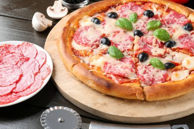 Lezzetli pizza, malzemeler ve siyah ahşap masa, yakın plan.
