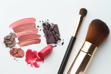 Beyaz arka planda farklı kozmetik ürünler ve makyaj fırçaları, düz yatış