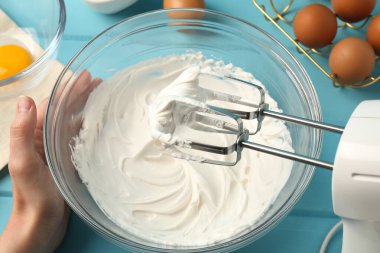Açık mavi ahşap masada el çırpıcı kremalı bir kadın.