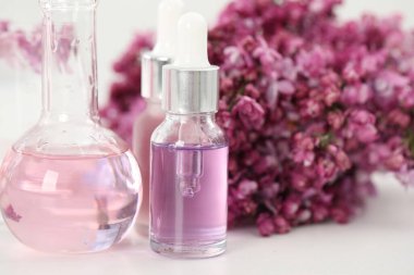 Lüks parfüm yapıyorum. Temel yağlar cam eşyalar ve çiçekler beyaz masada, yakın plan.