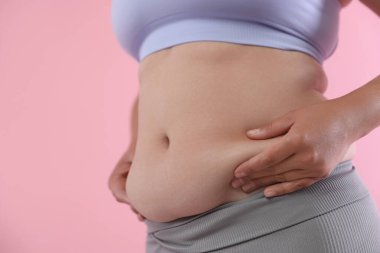 Pembe arka planda göbeği aşırı yağlı bir kadın, yakın plan. Aşırı kilolu