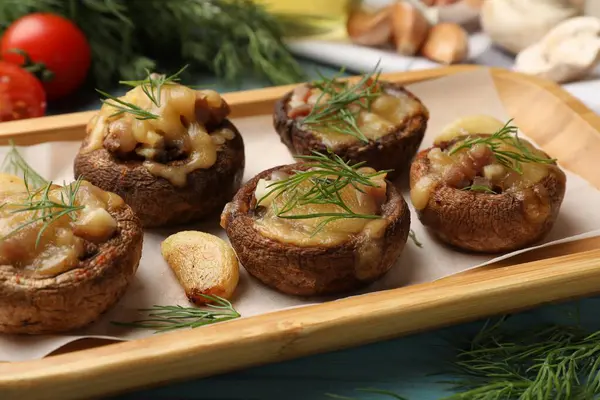Eritilmiş peynirli, sarımsaklı ve dereotlu leziz mantarlar açık mavi ahşap masada, yakın plan.