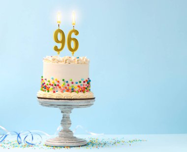 Üzerine şeker serpiştirilmiş lezzetli pasta, yanan numara şekilli mumlar ve açık mavi arka planda serebentin flama, yazı için yer. 96. yaş günü veya diğer özel günler