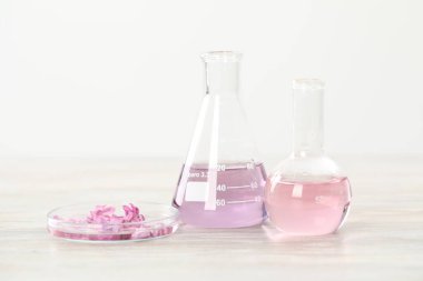 Lüks parfüm yapıyorum. Temel yağlar cam süslemede ve çiçekler beyaz ahşap masada, yakın plan.