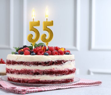 Böğürtlenli lezzetli pasta ve yanan mumlar ışık masasında. 55. yaş günü veya diğer özel günler