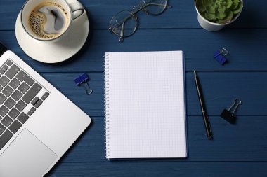 Kalemli, dizüstü bilgisayarlı, ataçlı ve mavi ahşap masadaki kahveli defter.