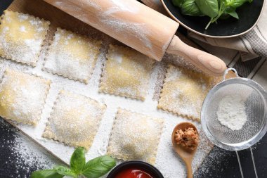 Pişmemiş ravioli, merdane, bolonez, sos ve fesleğen siyah masada, düz yatıyordu.