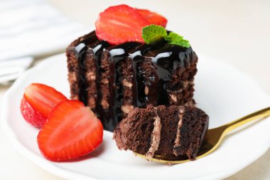 Çilek ve kaşıkla servis edilen bir parça çikolatalı pasta, yakın plan.