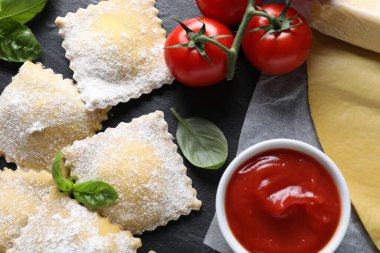 Pişmemiş ravioli, sos, domates ve fesleğen siyah masada, düz yerde.