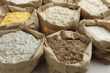 Beyaz masadaki kağıt torbalarda farklı türde un, yakın plan.