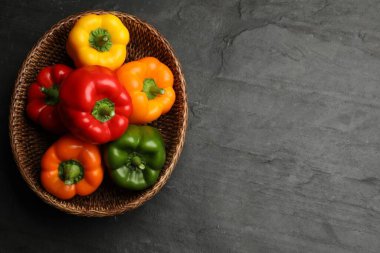 Hasır sepetin içinde taze renkli dolmalık biberler, siyah desenli masa, üst manzara. Metin için boşluk