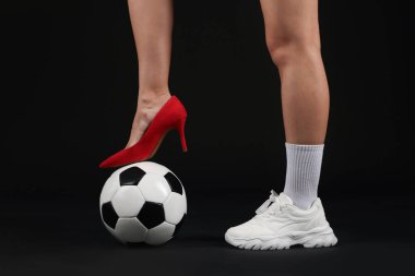 Arka planda futbol topu olan yüksek topuklu ayakkabılı ve spor ayakkabılı bir kadın.