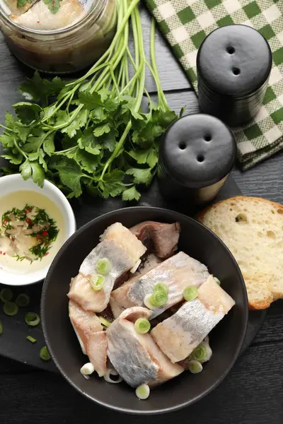 Lezzetli ringa balıkları. Siyah ahşap masa üzerinde yeşil soğanlar.