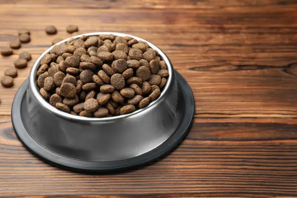 Tahta arka planda besleme kabında kurutulmuş hayvan mamaları, yakın plan.