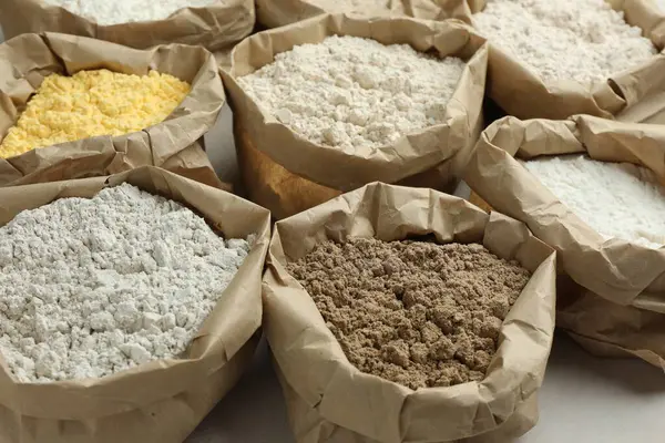 Beyaz masadaki kağıt torbalarda farklı türde un, yakın plan.