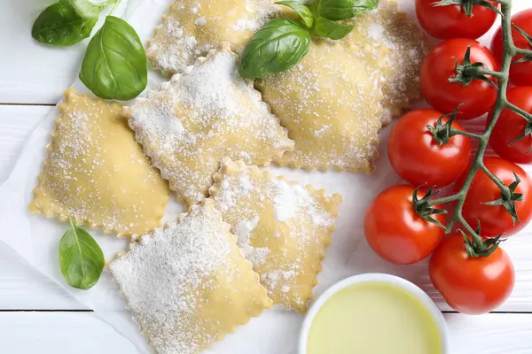 Pişmemiş ravioli, fesleğen, domates ve yağ beyaz ahşap masa üzerinde, düz uzanmış