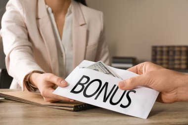 İşçi, ahşap masadaki patrondan bonusla zarf alıyor, yakın plan.